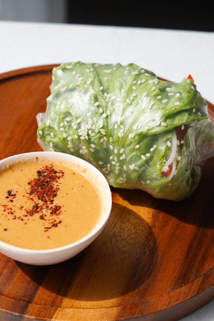 giant spring roll before cutting next to a serving of peanut sauce