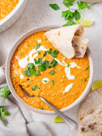 red lentil coconut curry served in a white bowl with naan, vegan cream and fresh herbs