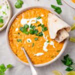 red lentil coconut curry served in a white bowl with naan, vegan cream and fresh herbs