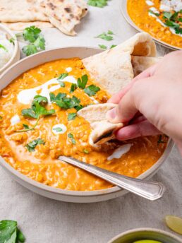 red lentil coconut curry with a spoon and naan dipped in