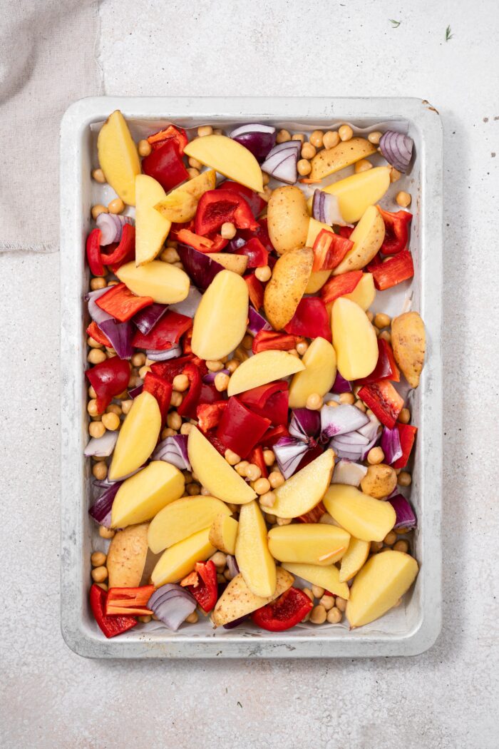 Potatoes, chickpeas, bell peppers, and red onions arranged on a baking sheet.