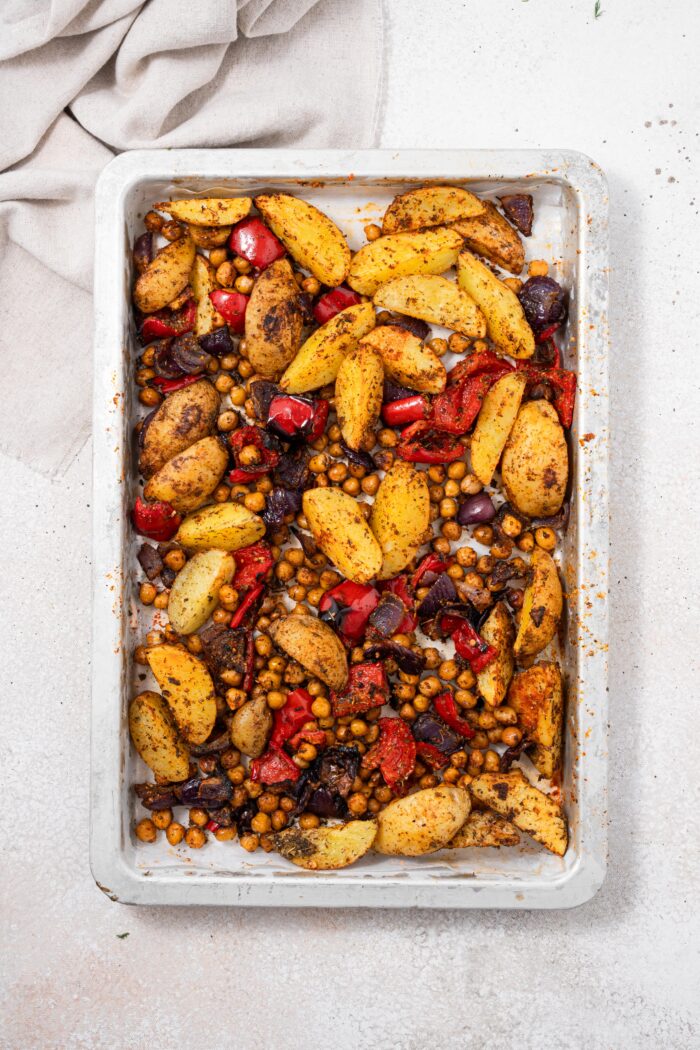 Roasted vegetables in a baking sheet , including potatoes, peppers, chickpeas , and red onions.