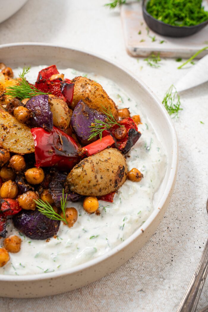 Close up shot of roasted vegetables served on a bed of vegan tzatziki.
