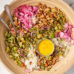 warm brussels sprouts salad ingredients in a mixing bowl with vinaigrette