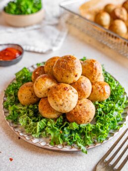 potato pops on a plate with green, condiment and more pops in the background