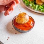 A single potato pop on a skewer dipped in ketchup.