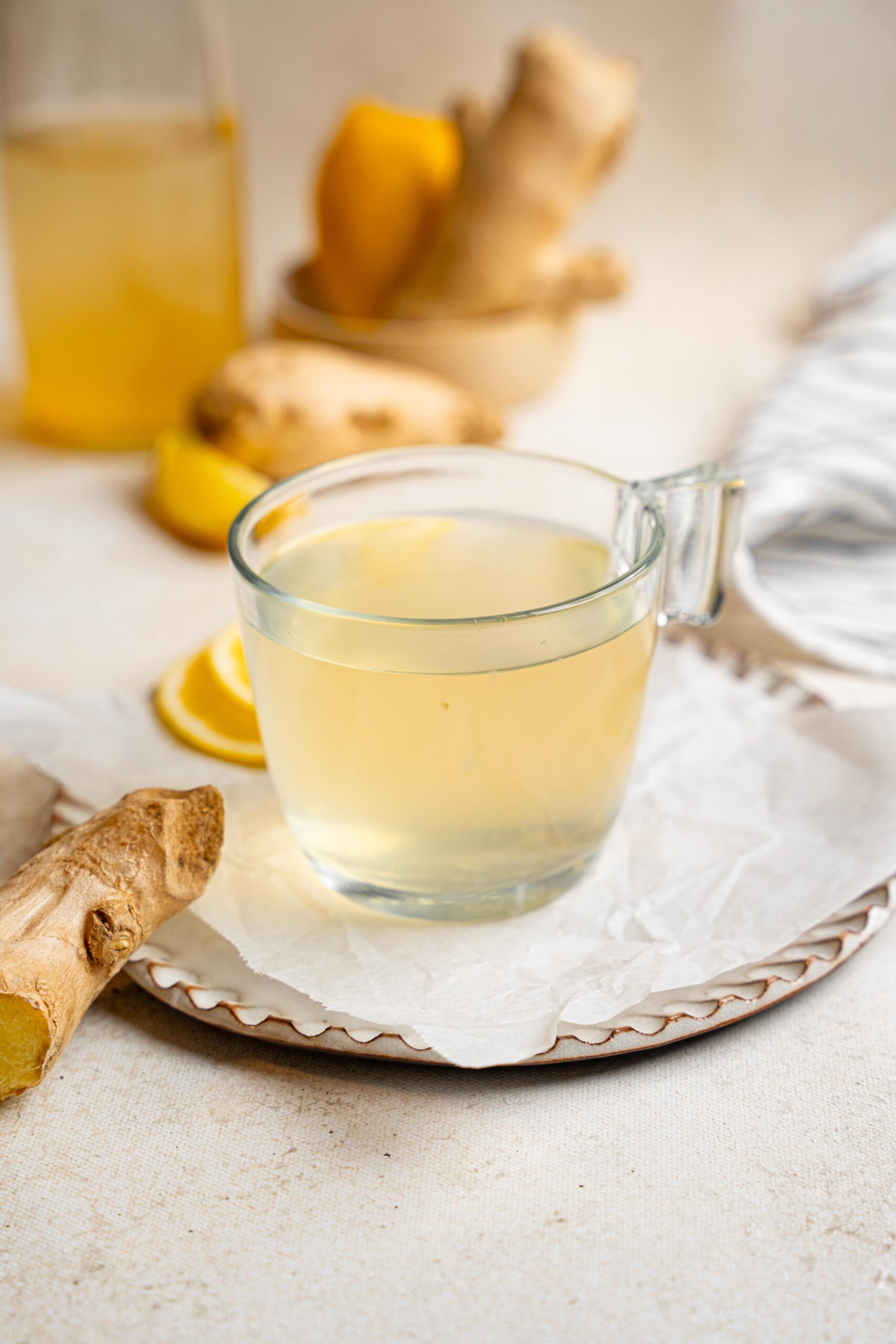switchel in a glass cup on a crinkled parchment and white saucer