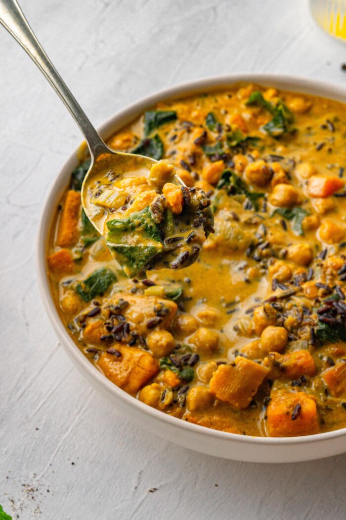 vegan creamy wild rice soup in a white bowl with a spoon