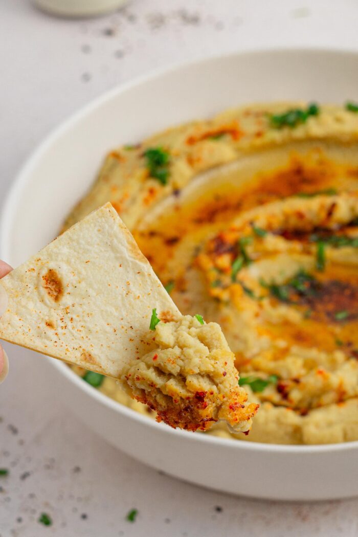 red lentil hummus on a tortilla chip resting ont he side of a bowl
