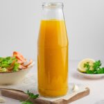 hidden veggie broth in a glass bottle with the ingredients in the bakcground