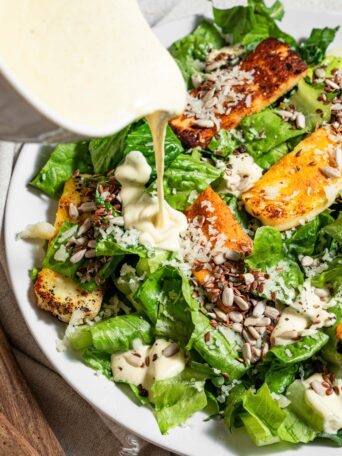 dressing being poured on vegan caesar salad