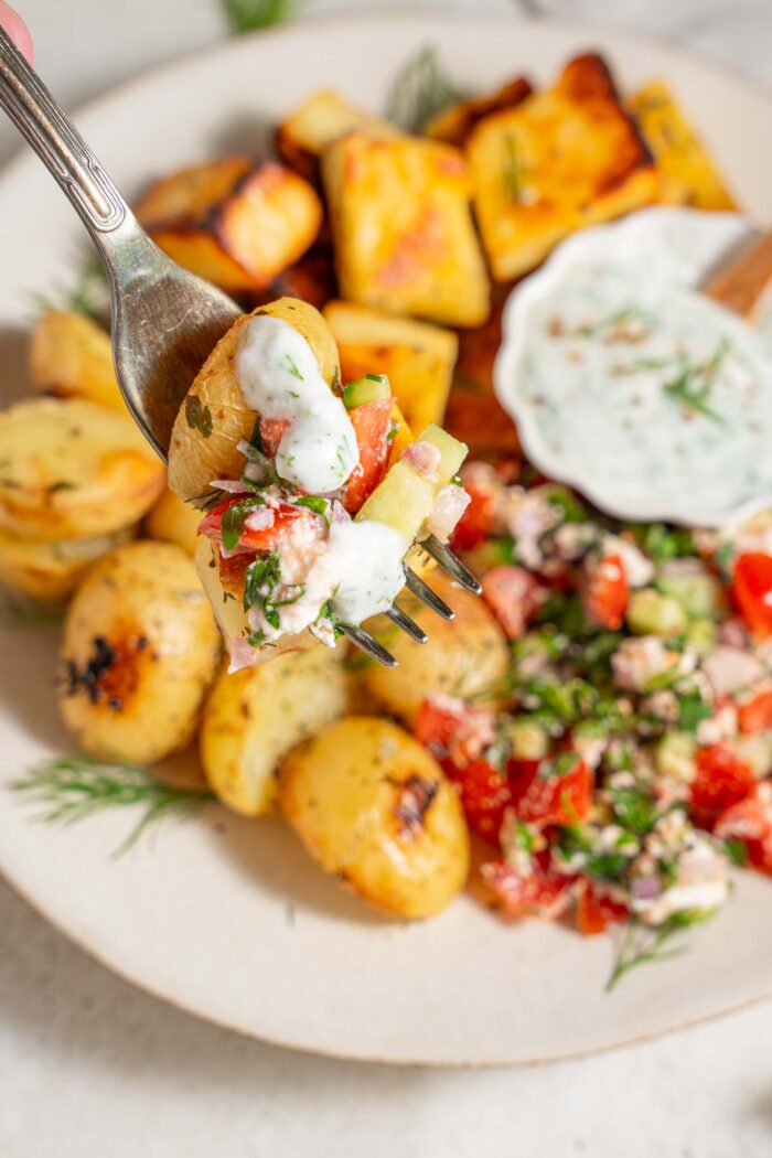 some potato, greek salad and yogurt dressing liften on a fork