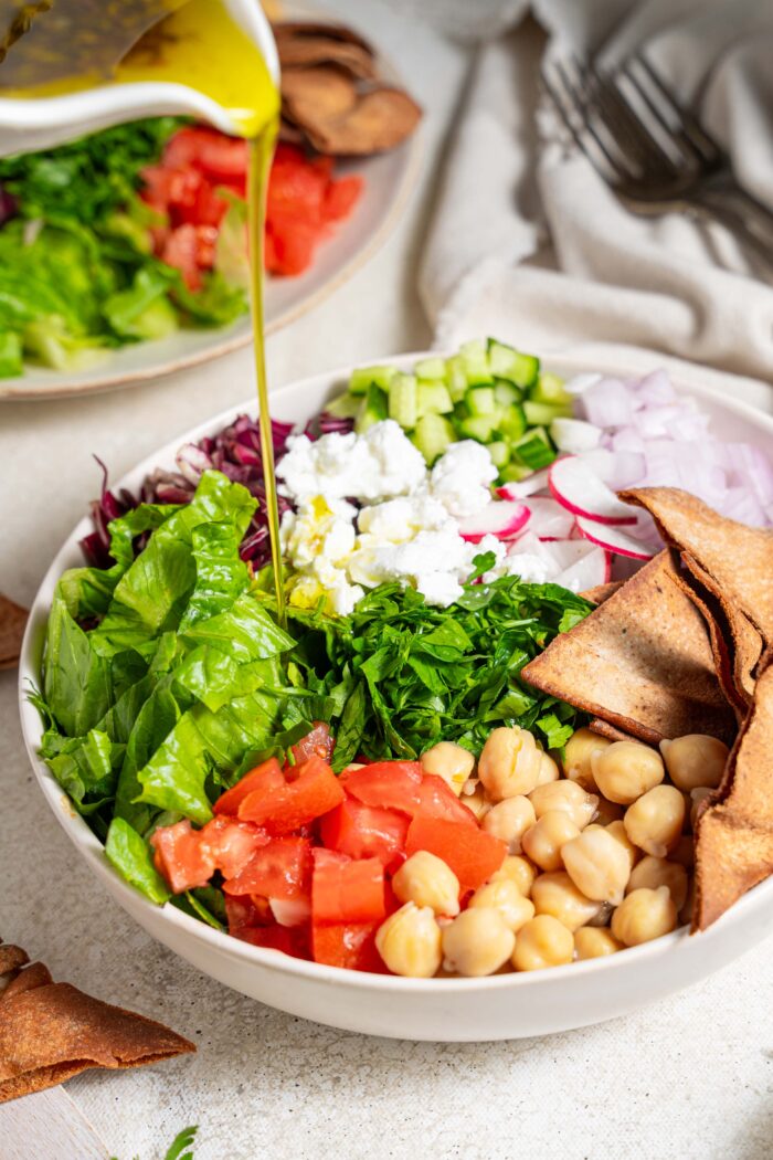 dressing being poured over fattoush salad with chickpeas
