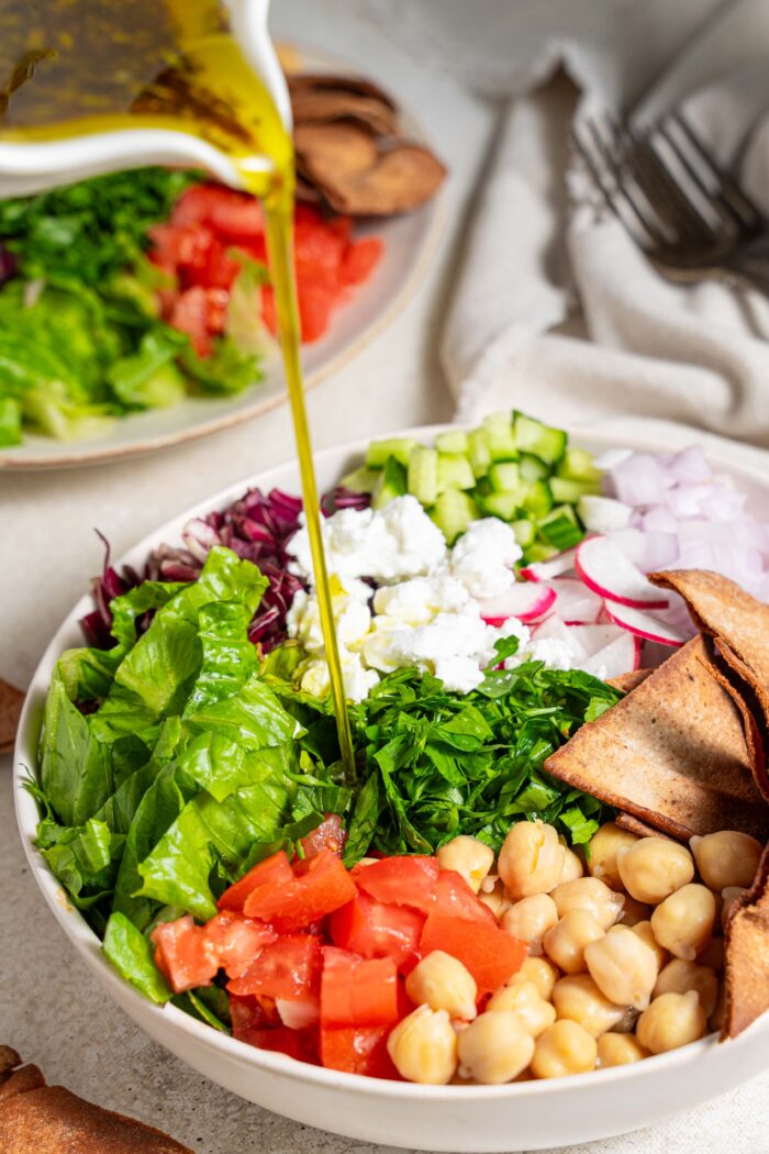dressing being poured over fattoush salad with chickpeas