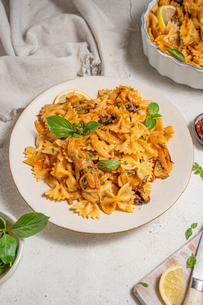 one pan caramelized onion pasta served on a white plate with fresh basil