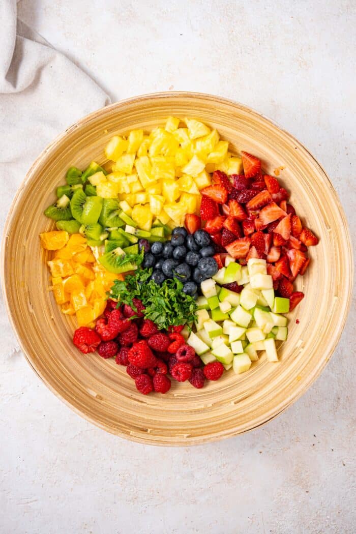 chopped fruit in a wooden salad bowl in a white background