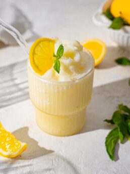 creamy iced lemonade with lemons and mint in the background