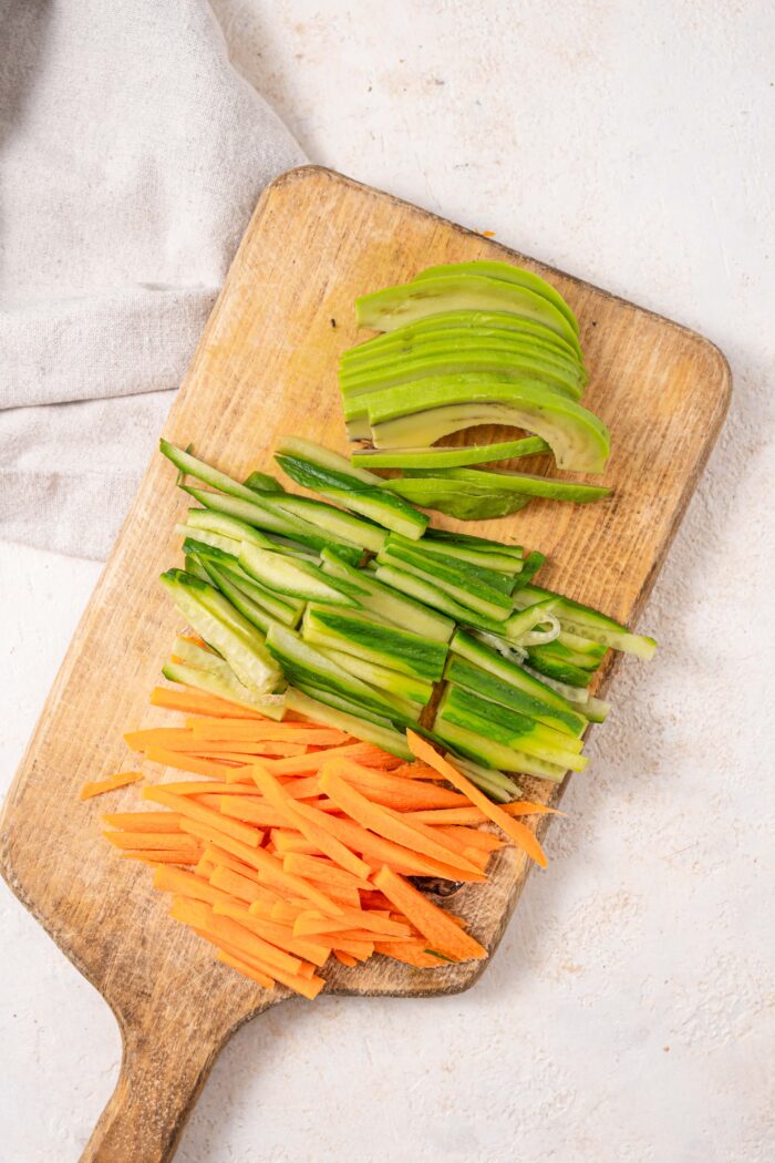 carrots, cucumber and avocado sliced and laid out on a cutting board