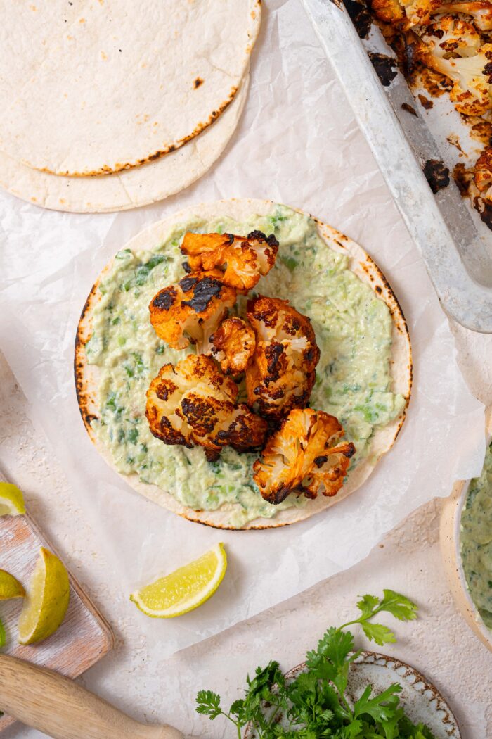 big florets of spicy cauliflower added on top of a tortilla and avocado crema