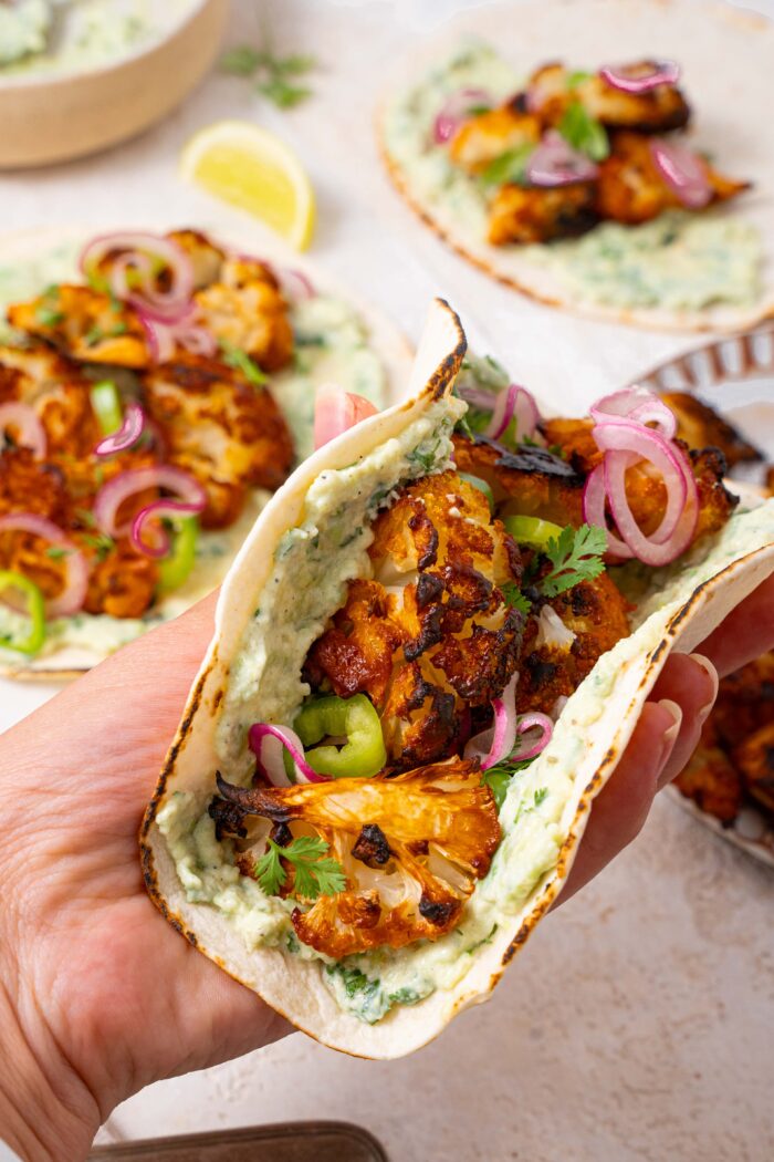 a hand holding delicious vegan spicy cauliflower tacos