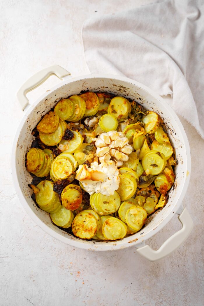 Roasted vegetables, garlic, and vegan cream cheese in a white casserole dish.