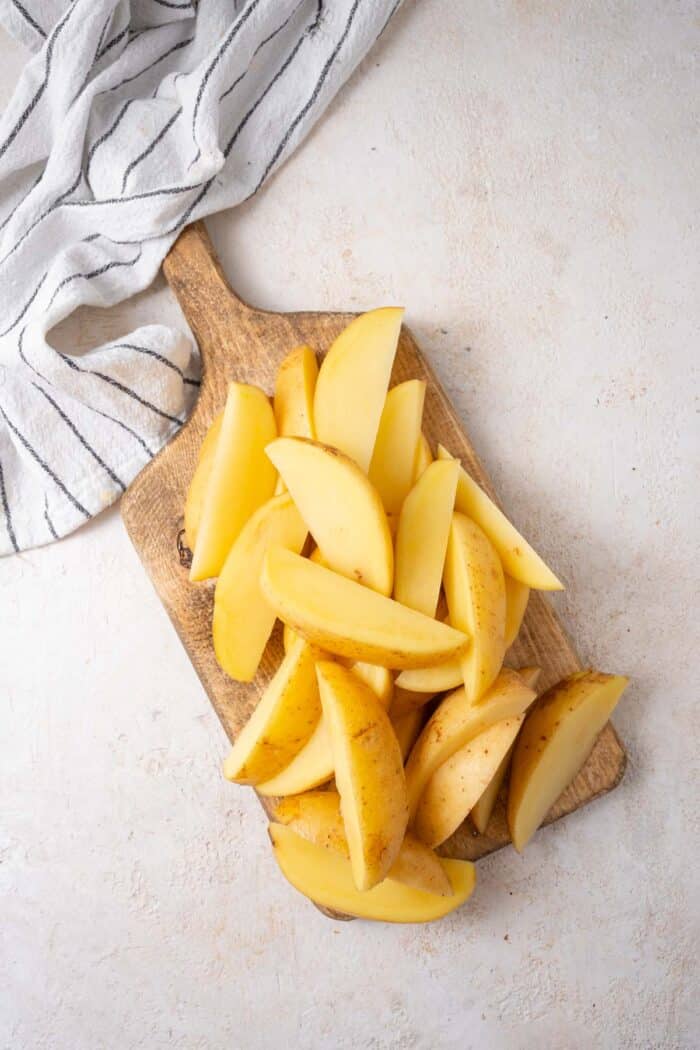 Yukon gold potatoes cut into long wedges and laid on a wooden cutting board.