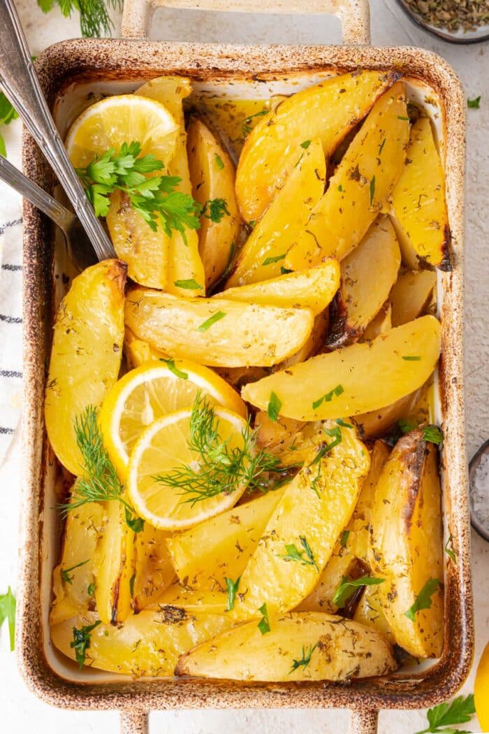 Top down shot of roasted vegan Greek potatoes with fresh herbs and lemon slices.