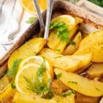 Greek potatoes close up with a couple of serving utensils visible.