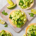 Green goddess salad tostadas served on a light wooden board with limes and pasley as garnish.