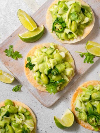Green goddess salad tostadas served on a light wooden board with limes and pasley as garnish.