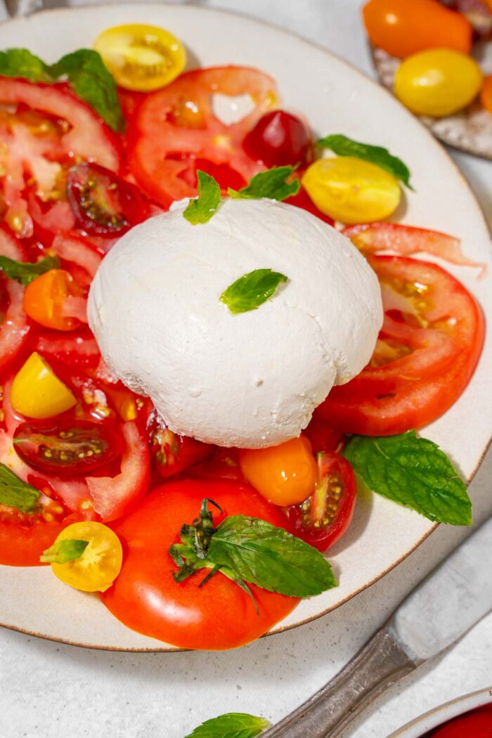 Closer look at the vegan burrata ball placed at the center of sliced tomatoes.