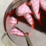 Lightly colored tea towels submerged in magenta colored dye and stirred with a metal spoon.
