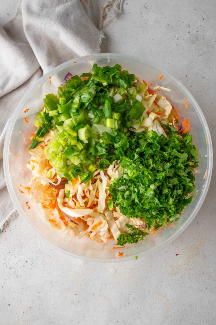 Coleslaw mix with cilantro and green onions in a mixing bowl.