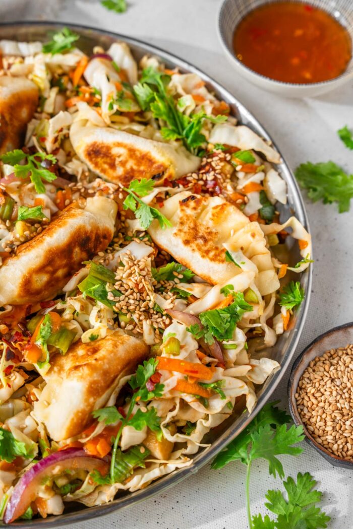 Dumpling salad served in a wide bowl, withs sesame seeds and chili oil as optional toppings.