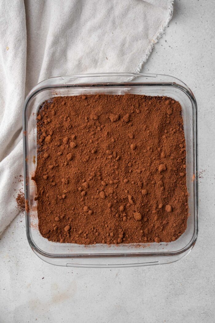Cocoa powder and sugar spread on top of cake batter in the pan.
