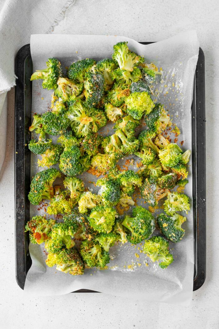 Broccoli with olive oil and spices on a baking sheet.