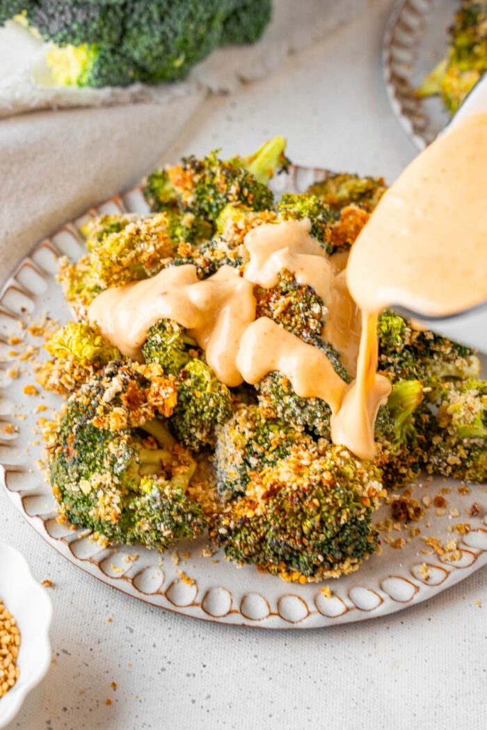 Bang Bang sauce being poured over the roasted broccoli.