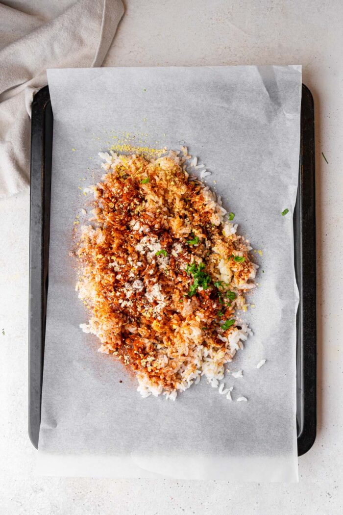 Cooked rice mixed with spices and seasonings on a lined sheet pan.