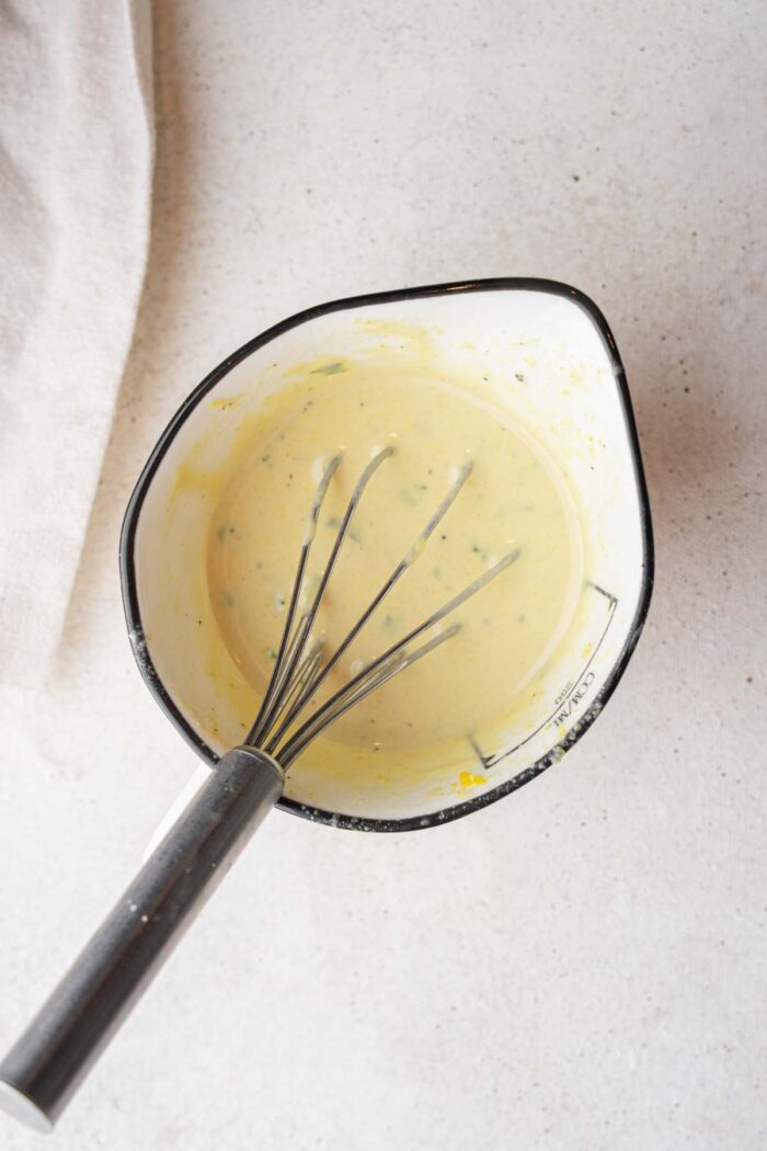 Tahini dijon dressing in a jug, with a whisk sticking out.