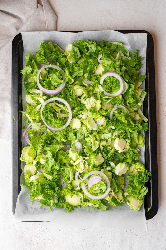 Brussels sprouts, kale, and onion spread on a lined sheet pan.