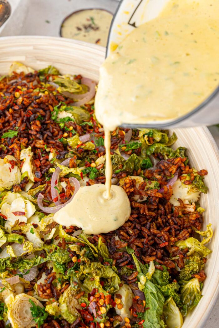 Dressing being poured into the salad bowl with the green base and crispy rice.