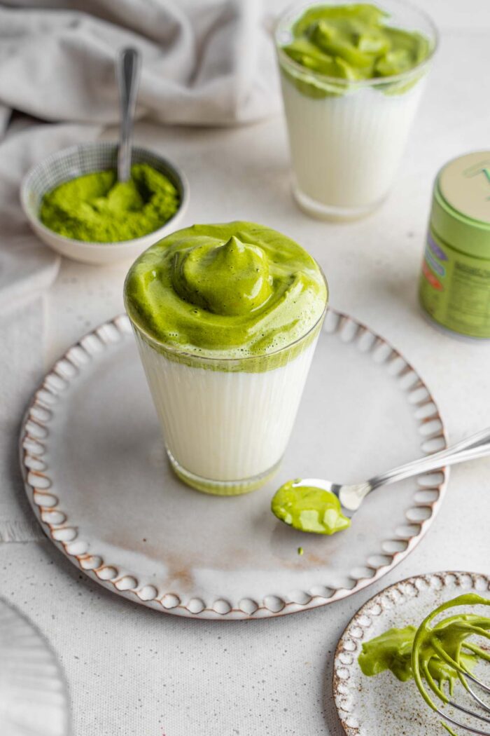 Dalgona matcha served in a glass atop of a plate.