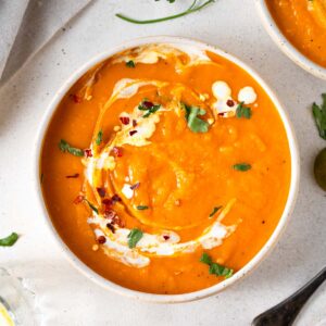 A bowl of golden butternut squash carrot soup with a swirl of coconut milk and fresh herbs.