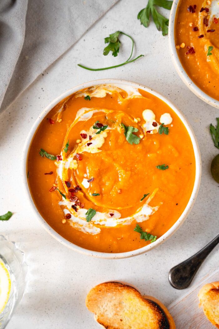 A bowl of golden butternut squash carrot soup with a swirl of coconut milk and fresh herbs.