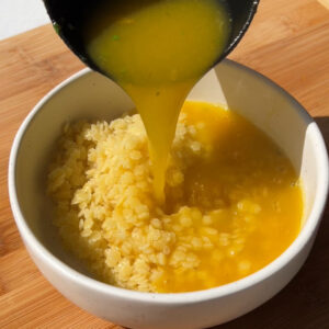 a clear broth soup being poured onto pastina