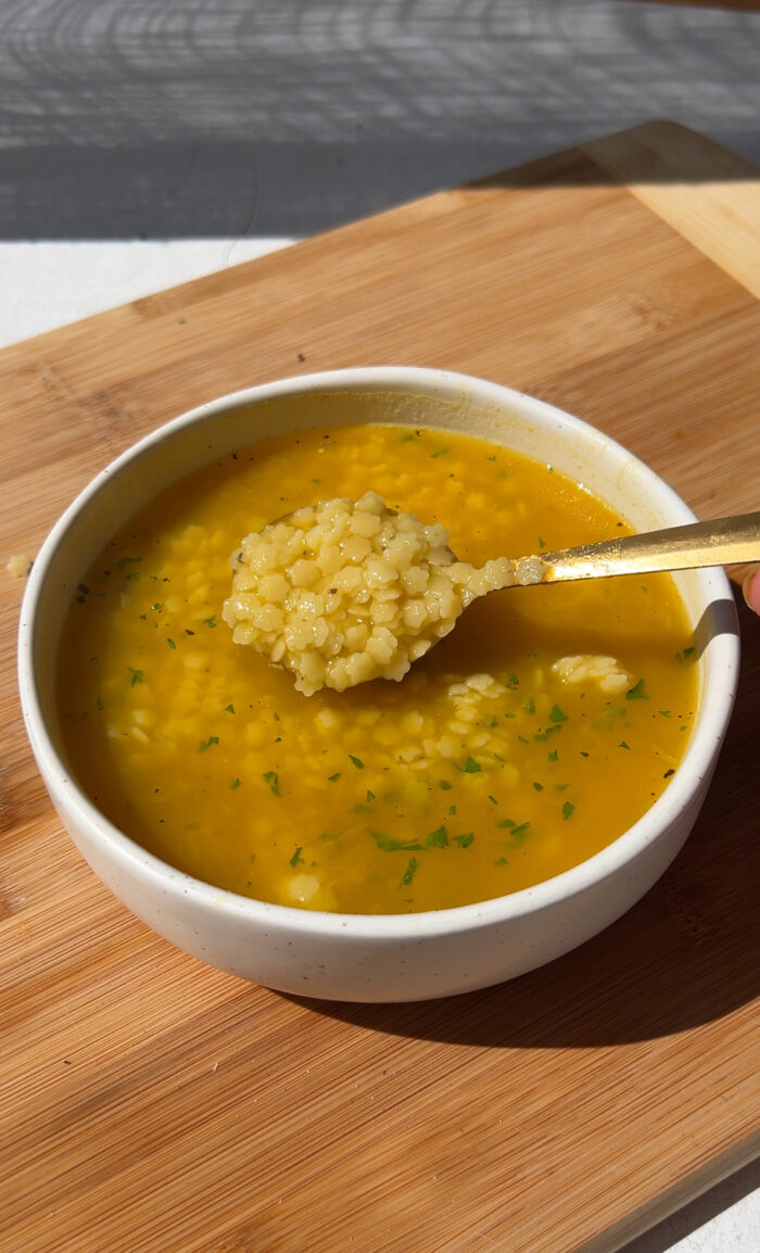 a clear broth soup being poured onto pastina 