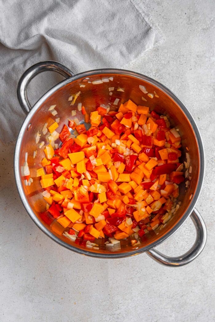 Sweet potato, onion, bell pepper, and garlic cooking together in a steel pot.