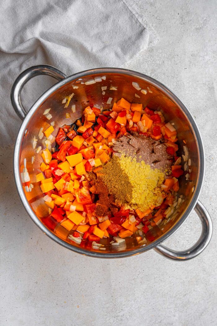 Spices, including chili, cumin, soy sauce, paprika, and nutritional yeast added to the pot.