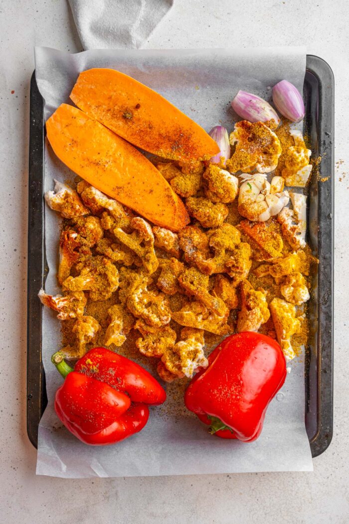 Raw vegetables with spices on a sheet pan.