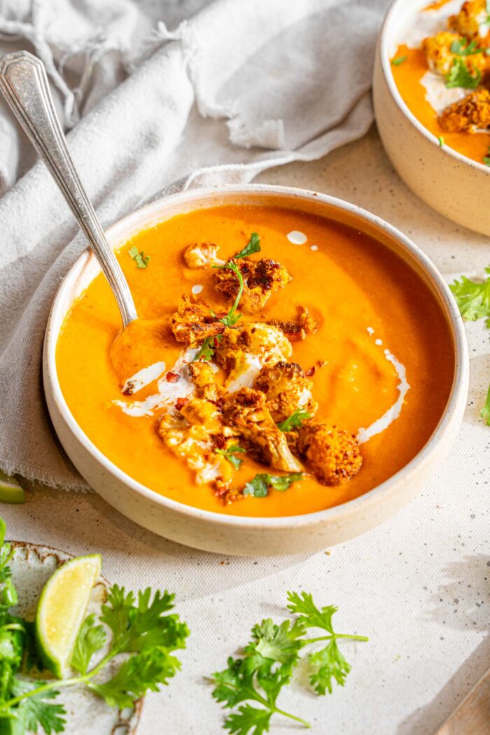 Sweet potato cauliflower soup served in a white bowl with roasted cauliflower, parsley, and a drizzle of coconut milk.